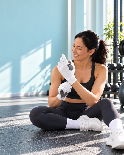 Sitting against a pale blue wall, pulling on a white HOLD glove before training.