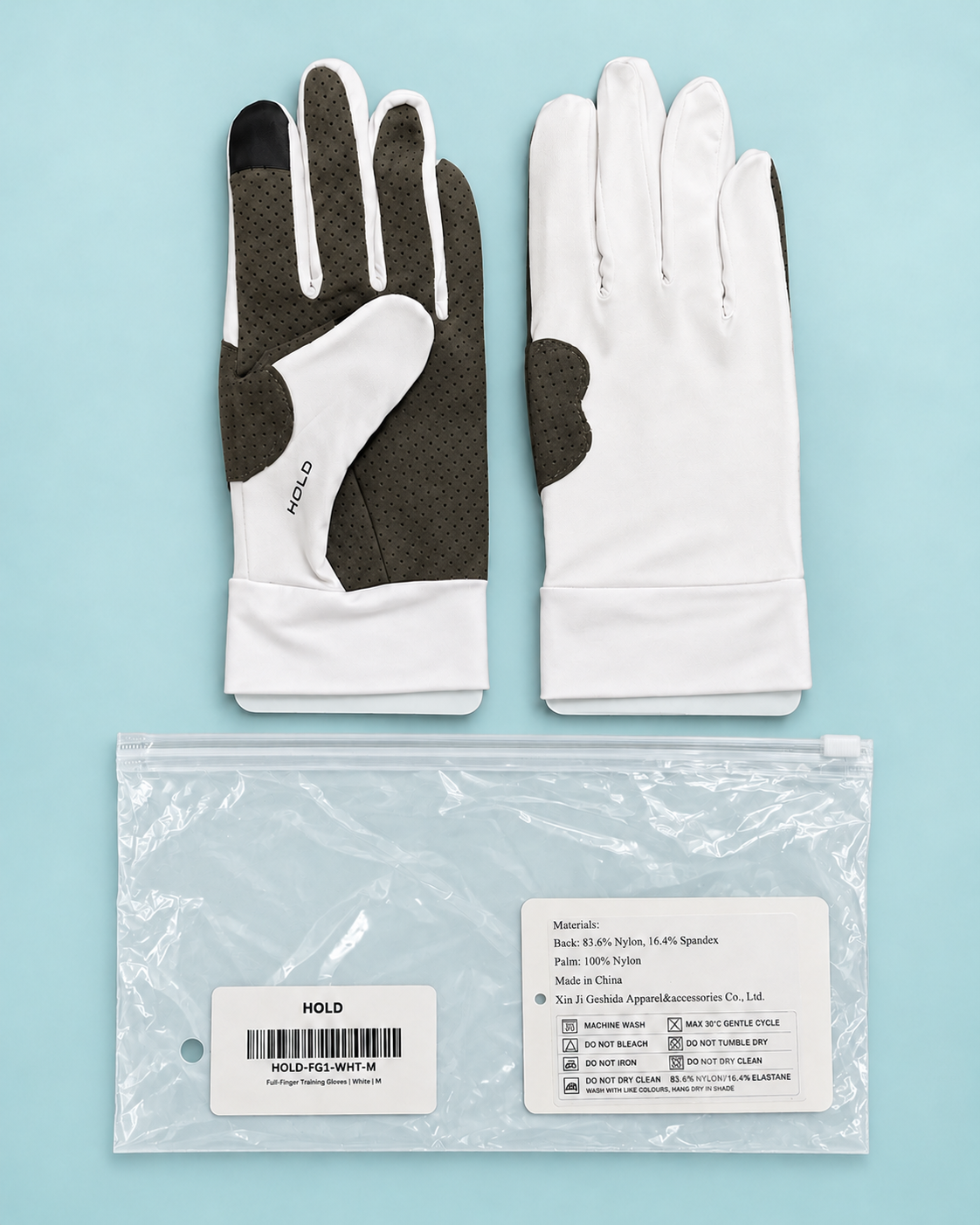 Both HOLD gloves laid flat beside the resealable bag they ship in, with the care and size label visible.